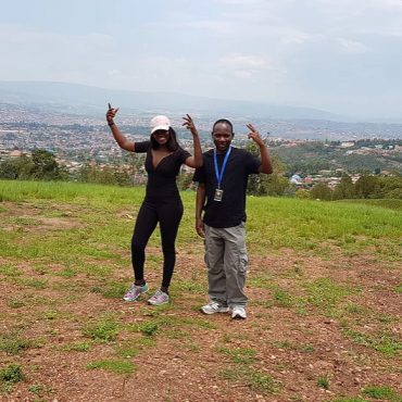 Two guides posing on a grassy hill above a city in Rwanda